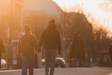 Lovely couple is walking into the orange sunset on the avenue in berlin, holding hands and...