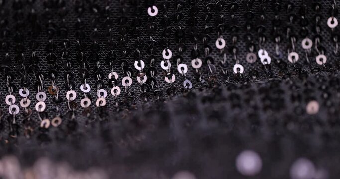 a large number of sequins on a black material, a part of the black material decorated with plastic discs to create shine