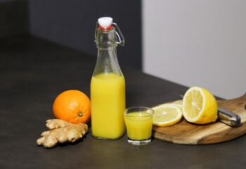 Homemade orange, lemon and ginger drink in a glass bottle with a small shot glass 