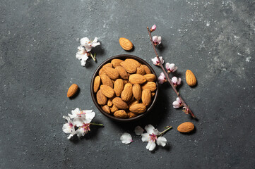 Fresh Raw Sweet almonds in wooden bowl or shovel with almond tree flowers on rustic background, nut, healthy food