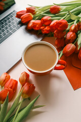 Cup of coffee, bouquet of red tulips and laptop top view flat lay, festive background