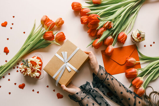 Gift box with a bow and tulips in the hands of a girl, festive background