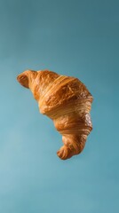 A croissant suspended in the air with a clear blue sky in the background.