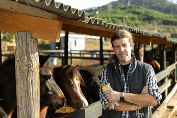 Portrait of man next to pony in stall at stable on a summer day