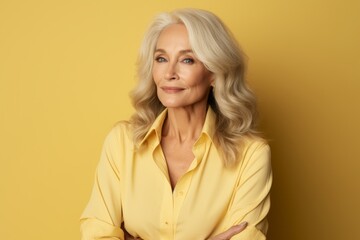 Portrait of beautiful mature woman in yellow shirt over yellow background.