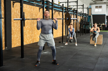 Adult male bodybuilder performing strength and endurance exercises during group barbell lifting in...