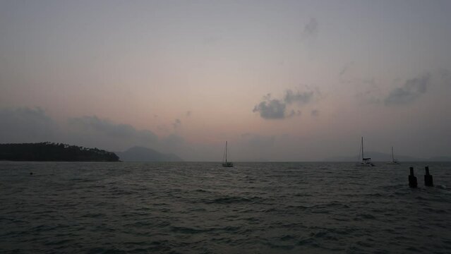 February 1, 2024 - Rawai, Phuket Thailand. Sunrise viewed from the landing pier with sailboats anchored in the water.