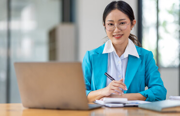 Portrait of asian young female entrepreneur sitting at her desk in the office - obrazy, fototapety, plakaty