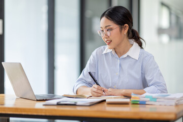 Asian Businesswoman Using laptop computer and working at office with calculator document on desk, doing planning analyzing the financial report, business plan investment, finance analysis concept.
