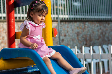 Fototapeta na wymiar little brunette latina girl sitting on top of small slippery slide about to slide down