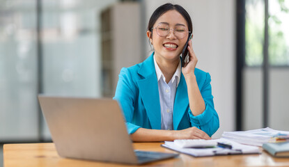 Cheerful business Asian woman freelancer making telephone call share good news about project working in office workplace, business finance concept.	