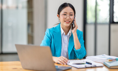Fototapeta premium Cheerful business Asian woman freelancer making telephone call share good news about project working in office workplace, business finance concept. 