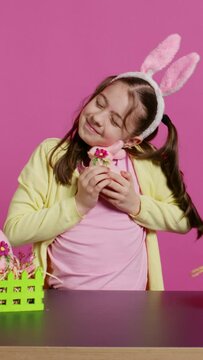 Cheerful smiling girl hugging her stuffed rabbit toy and egg, feeling proud about her handcrafted painted easter decorations. Young toddler with bunny ears and pigtails, festive ornaments. Camera B.