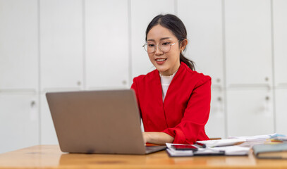 Portrait of Happy young business asian woman in red suit sitting at her desk in the office business finance concept.	