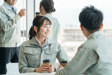 オフィスの休憩所でコーヒーを飲む作業着姿の女性と男性
