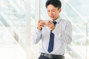 オフィスで休憩中にスマホでゲームする若いアジア人ビジネスマン
