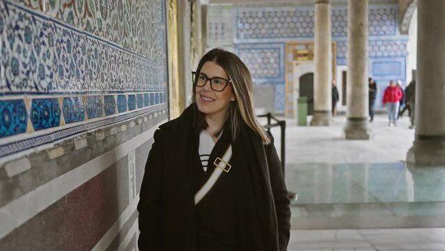 A smiling woman explores the historic topkapi palace in istanbul, surrounded by ancient tilework and architecture.