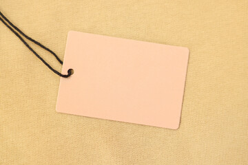 Cardboard tag on beige garment, top view. Space for text