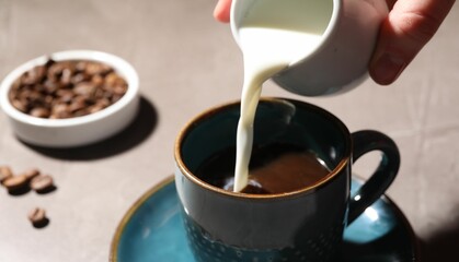 Woman pouring milk into cup with aromatic coffee at light table, closeup