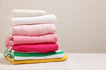 Stack of folded clothes on wooden table against grey background, space for text