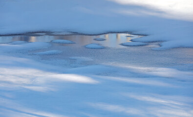 The edge of melting ice and reflection of bare birch trees 