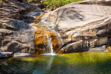 A rockslide cascade and waterfall flowing into a swimming hole rock pool over granite bedrock in Paluma National Park, a popular tourist attraction near Townsville in Queensland, Australia.