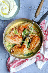 Chicken dish with dijon mustard sauce in a copper pan with herb garnish on light, portrait style on grey background with red striped tea towel