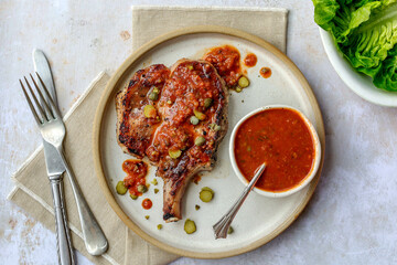 Grilled pork chop with tangy sauce, a bistro classic presented as an overhead, landscape  shot on a...