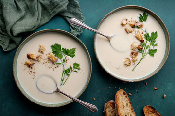 Traditional cauliflower and potato soup served in two green bowls with croutons and parsley on a...