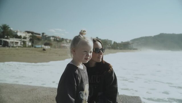 Young mother and baby daughter looking out to sea. Slow motion 120