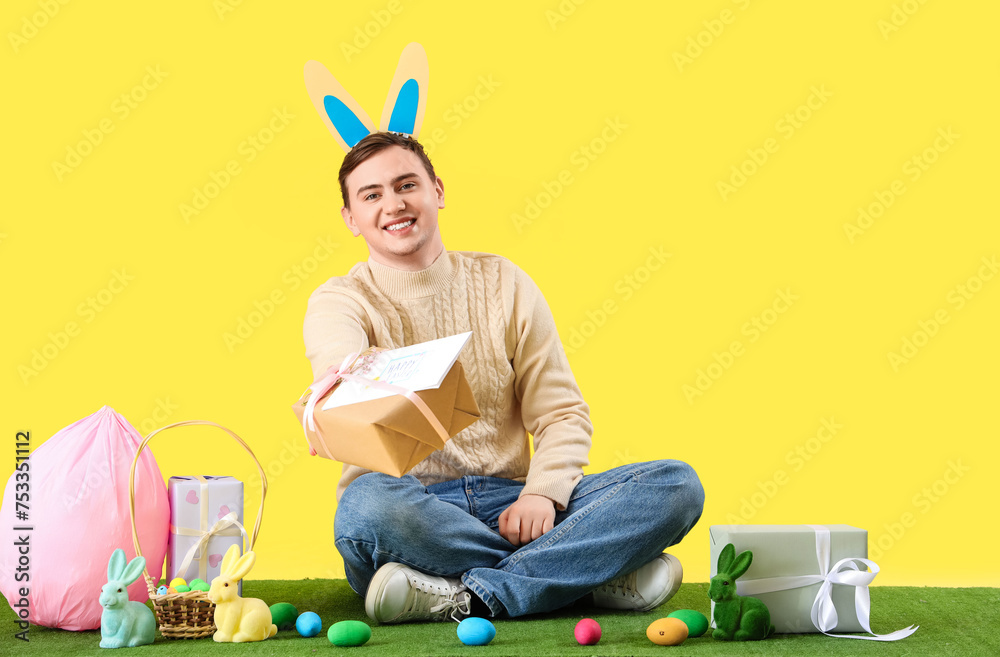 Sticker Happy young man in bunny ears with gift boxes and Easter eggs celebrating on yellow background