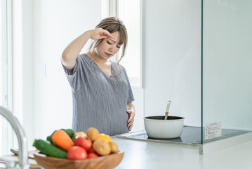 妊娠中にキッチンで調理中に体調不良になる女性（頭痛・発熱）
