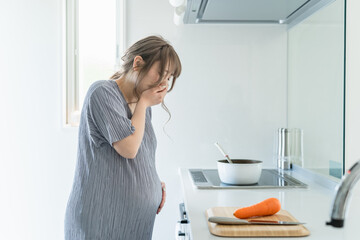 キッチンで吐き気・悪阻・嘔吐に苦しむ妊婦の女性
