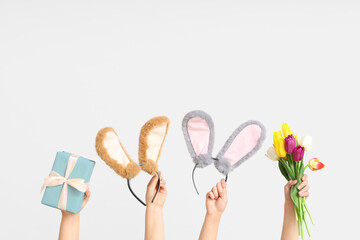 Female hands holding Easter bunny ears headbands with gift box and tulips on white background