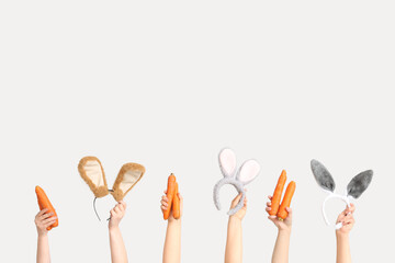 Female hands holding Easter bunny ears headbands and carrots on white background