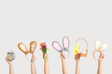Female hands holding Easter bunny ears headbands with basket, alarm clock and tulips on white background