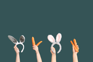 Female hands holding Easter bunny ears headbands and carrots on dark green background
