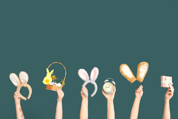 Female hands holding Easter bunny ears headbands with gift box, basket and alarm clock on dark...