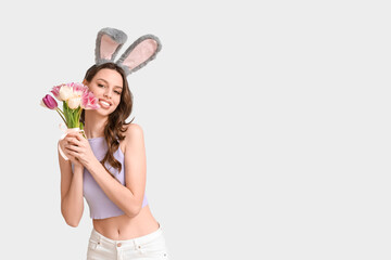 Happy young woman in Easter bunny ears headband with bouquet of tulips on white background
