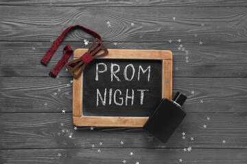 Chalkboard with text PROM NIGHT, bow tie and perfume bottle on grey wooden background