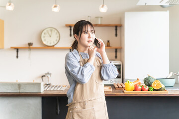 家のキッチン・ダイニングでスマホで電話しながら驚くアジア人女性
