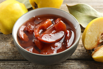 Tasty homemade quince jam in bowl and fruits on wooden table, closeup