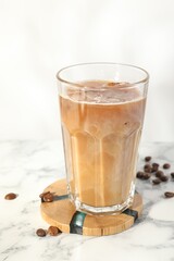 Refreshing iced coffee with milk in glass and beans on white marble table