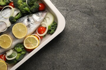Raw fish with vegetables and lemon in baking dish on grey textured table, top view. Space for text