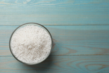 Raw basmati rice in bowl on light blue wooden table, top view. Space for text