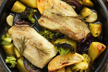 Pieces of delicious baked cod with vegetables, lemon and spices in dish, top view