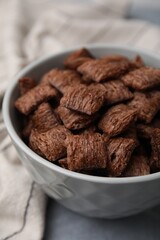 Chocolate cereal pads in bowl on grey table, closeup