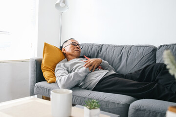 Elderly Asian man wear glasses, sleeping on couch at home after tired reading a book
