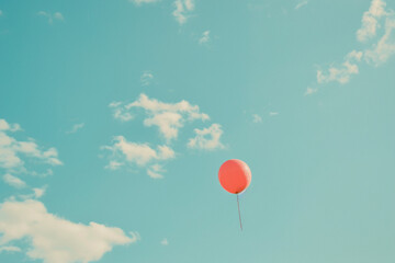 A red balloon soars against a blue sky with clouds.