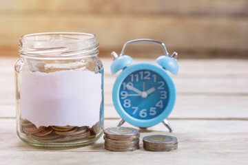 Coins,alram clock and pencil with empty notebook on wood table background.